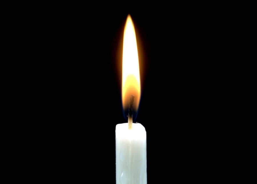 Sexstellung Kerze: Eine weiße Kerze mit heller Flamme auf schwarzem Hintergrund